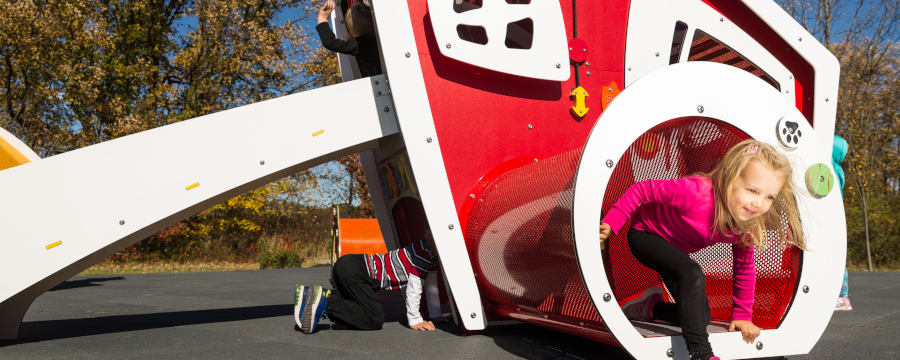 Young girl crawling through tube on an early childhood playground.