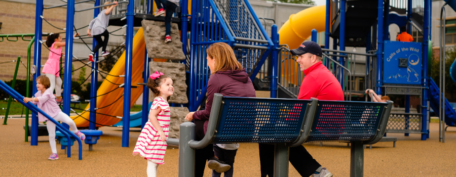 Children playing on a playground while parents watch from a bench