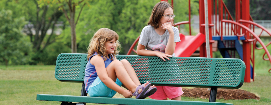 Two girls hanging out at a park bench
